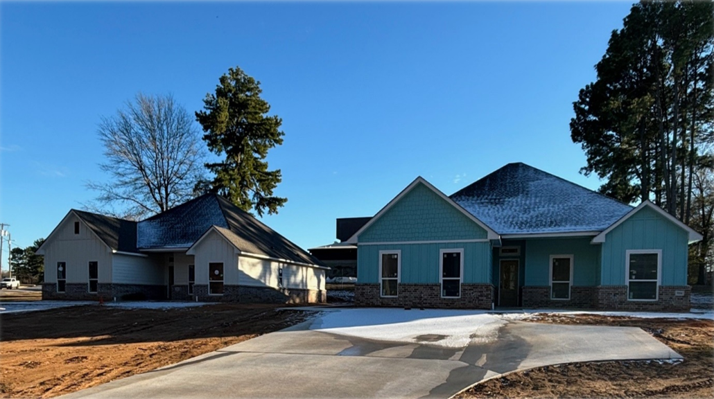 Newly constructed homes with mixed siding colors under a clear blue sky and driveways leading up to the homes.