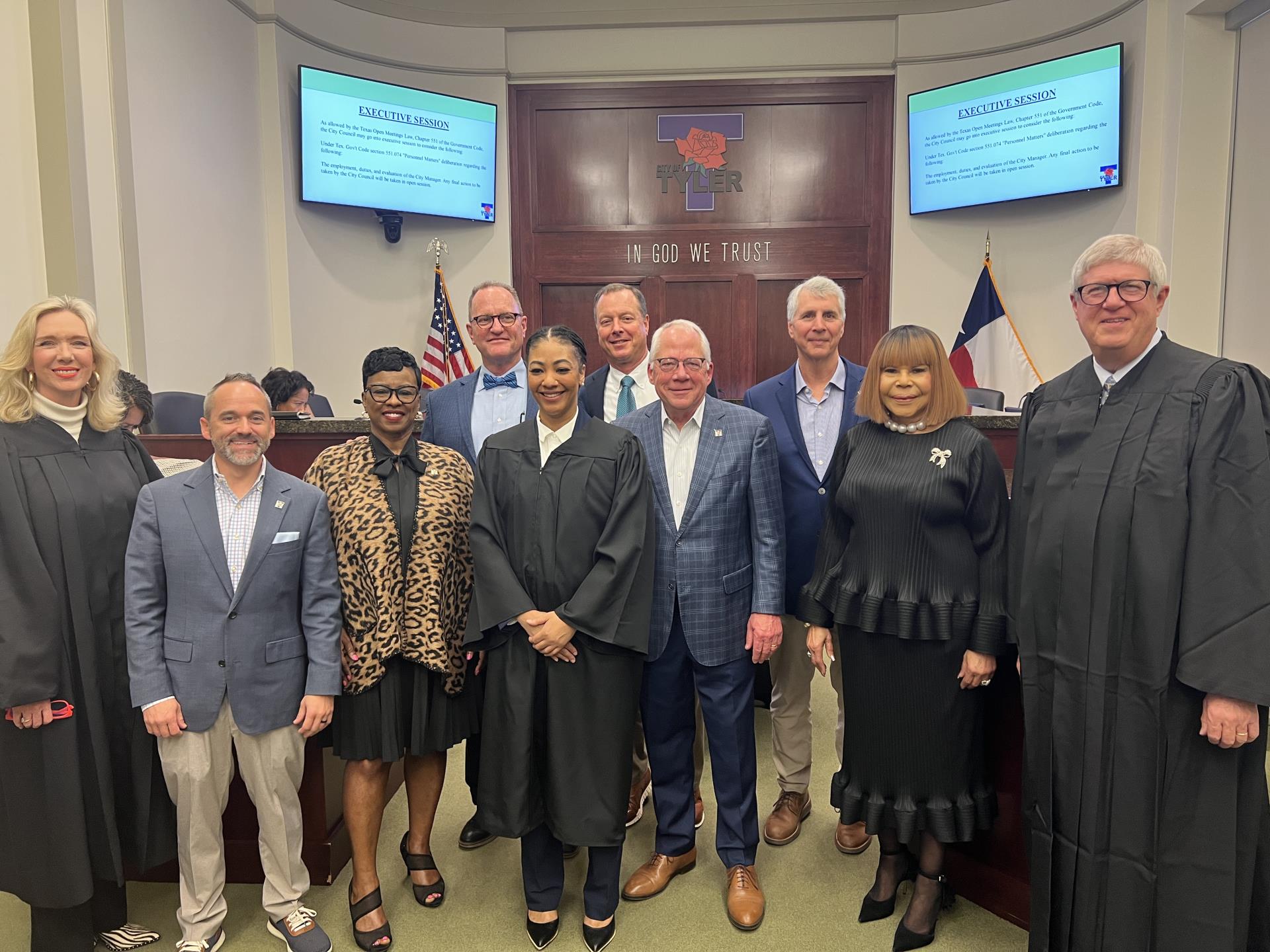 A group photo featuring judges and city officials. Three individuals wear black judicial robes, while others are dressed in business attire, including blazers, suits, and a leopard-print jacket.